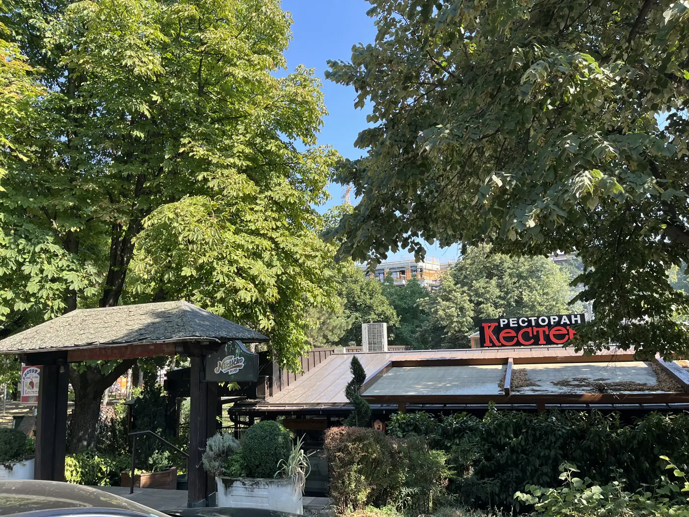Ulaz u restoran Kesten sa ulice — drvena kapija sa nadstrešnicom i tabla restorana među krošnjama kestenova